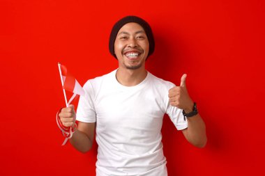 Endonezya gençliği, 17 Ağustos 'ta Endonezya Bağımsızlık Günü' nü kutlarken ve kırmızı zemin üzerinde izole edilmiş Endonezya bayrağını tutarken kameraya olumlu bir hareket gösteriyor.