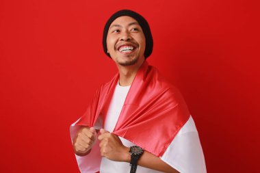 Endonezya Bağımsızlık Günü 'nü kutlamak için Endonezya bayrağını taşıyan mutlu ve heyecanlı bir Endonezyalı. Kırmızı arkaplanda izole edilmiş.