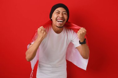 Endonezya Bağımsızlık Günü 'nü kutlamak için Endonezya bayrağını taşıyan mutlu ve heyecanlı bir Endonezyalı. Kırmızı arkaplanda izole edilmiş.