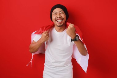 Endonezya Bağımsızlık Günü 'nü kutlamak için Endonezya bayrağını taşıyan mutlu ve heyecanlı bir Endonezyalı. Kırmızı arkaplanda izole edilmiş.