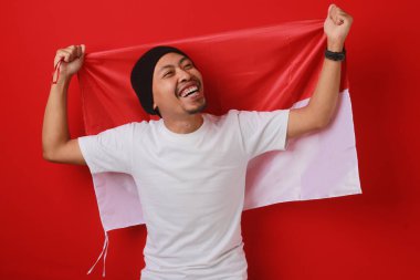 Endonezya Bağımsızlık Günü 'nü kutlamak için Endonezya bayrağını taşıyan mutlu ve heyecanlı bir Endonezyalı. Kırmızı arkaplanda izole edilmiş.