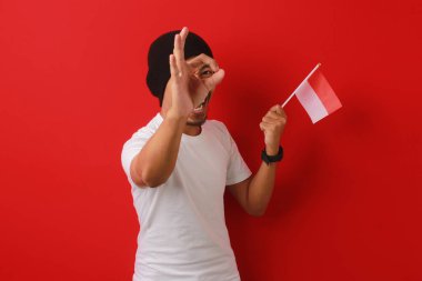 Heyecanlı Endonezyalı gençler 17 Ağustos 'taki Bağımsızlık Günü kutlamalarında kameraya bakarken ve Endonezya bayrağını tutarken, kırmızı arka planda izole edilmiş bir şekilde tamam bir jestten bakıyorlar.