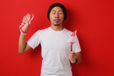 Endonezyalı adam, Endonezya Bağımsızlık Günü kutlamaları sırasında 17 Ağustos 'ta kırmızı bir arkaplanda izole edilmiş, beyaz gömlek ve bereli bir şekilde söz veriyor..