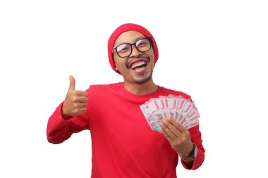 Endonezyalı kırmızı gömlekli adam, Endonezya 'nın 17 Ağustos' taki Bağımsızlık Günü 'nde elinde beyaz bir arkaplanda izole edilmiş Endonezya Rupiah banknotlarını tutarken olumlu bir jest yapıyor.
