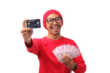 Endonezya 'nın 17 Ağustos' taki Bağımsızlık Günü kutlamaları sırasında elinde kredi kartı ve para tutan kırmızı uzun kollu gömlek ve kırmızı bere giyen mutlu Endonezyalı adam beyaz bir arka planda izole edilmiş.