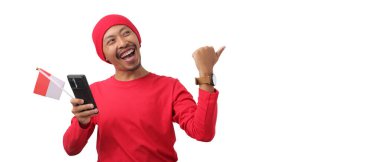 Endonezya Bağımsızlık Günü kutlamaları sırasında elinde Endonezya bayrağı ve telefonu tutarken, Endonezya 'nın kırmızı uzun kollu gömleği boş fotokopi alanını işaret ediyor. 17 Ağustos' ta beyaz arka planda izole edilmiş.