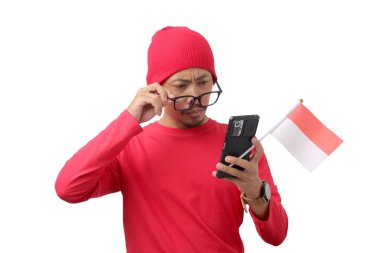 Endonezya Bağımsızlık Günü kutlamaları sırasında 17 Ağustos 'ta beyaz arka planda izole edilmiş, kafası karışmış Endonezyalı genç adam telefonuna dikkatle bakar.