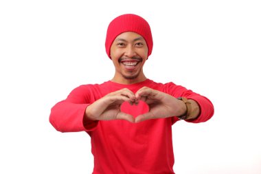 Endonezyalı uzun kollu, bereli bir adam Endonezya bayrağını tutarken ve 17 Ağustos 'ta Endonezya Bağımsızlık Günü' nü beyaz arka planda kutlarken kalp hareketi yapıyor.