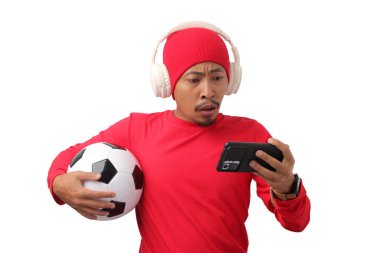 Endonezyalı uzun kollu kırmızı tişört giyen ve kulaklık takan bir adam, milli takımının maçına telefonuyla tepki veriyor.