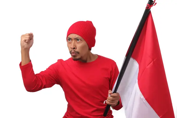 stock image Indonesian man wearing a red long sleeve T-Shirt gives a speech while holding an Indonesian flag and raising his fist in celebration of Indonesia's Independence Day on 17 August, on white background