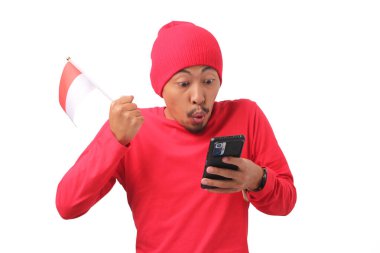 Endonezyalı kırmızı uzun kollu tişört ve kırmızı ve beyaz kurdeleli bere giyen adam, Endonezya Bağımsızlık Günü 'nde telefonundan iyi haberler alırken mutlu oluyor. Beyaz bir arkaplanda izole edilmiş