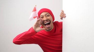 Kırmızı tişörtlü ve bereli heyecanlı Endonezyalı beyaz bir duvarın arkasından bağırarak, Endonezya Bağımsızlık Günü tanıtımı sırasında özel bir teklif veya indirim ilan etti. Beyaz bir arkaplanda izole edilmiş.