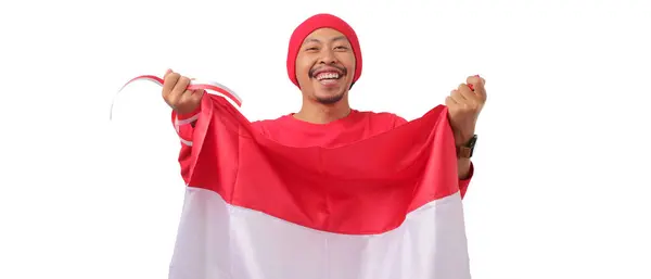 stock image Happy Indonesian man wearing a red long sleeve T-Shirt and a red beanie hat holds Indonesia's flag to celebrate Indonesia Independence Day on August 17. Isolated on a white background.