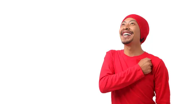 stock image Happy Indonesian man in a red long sleeve T-shirt and beanie hat, with Indonesia flag, puts his hand on his chest while listening to the Indonesia national anthem. Isolated on white background