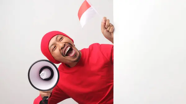 stock image Indonesian man in a white T-shirt shouts loudly while holding a megaphone behind a white wall. He is announcing special offers or discounts during Indonesia Independence Day special promotion