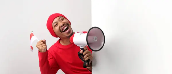 stock image Indonesian man in a white T-shirt shouts loudly while holding a megaphone behind a white wall. He is announcing special offers or discounts during Indonesia Independence Day special promotion