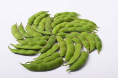 Taze edamame kapsülleri beyaz bir arkaplana karşı girdap şeklinde dizilmiştir.