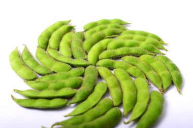 Taze edamame kapsülleri beyaz bir arkaplana karşı girdap şeklinde dizilmiştir.