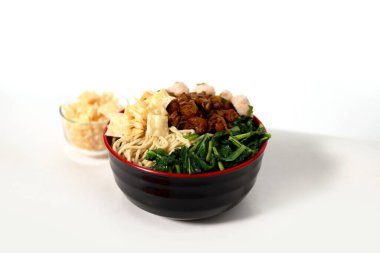 Bir kase Mie Ayam, tipik bir Endonezya yemeği, tavuklu erişte, doğranmış tavuk, köfte, köfte, yeşil sebze ve çeşitli malzemeler, beyaz bir arka planda izole edilmiş.