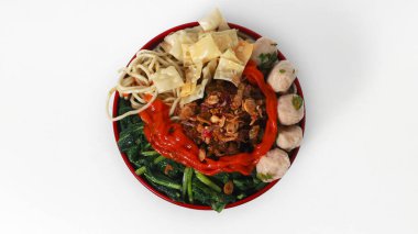 Bir kase Mie Ayam, tipik bir Endonezya yemeği, tavuklu erişte, doğranmış tavuk, köfte, köfte, yeşil sebze ve çeşitli malzemeler, beyaz bir arka planda izole edilmiş.