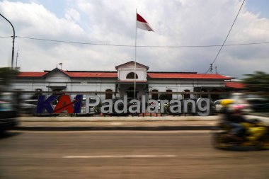 Bandung, Batı Java, Endonezya - Ekim 04, 2024: Endonezya 'daki Padalarang İstasyonu manzarası, Endonezya bayrağı istasyon önünde gururla dalgalanmaktadır. Arabalar ve bir motosiklet geçiyor.