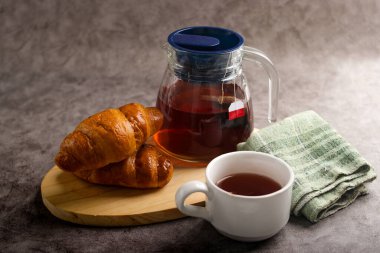 Sıcak bir kahvaltı sahnesi, yeni pişmiş kruvasanlar ve sıcak bir fincan çay.