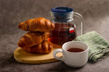 Sıcak bir kahvaltı sahnesi, yeni pişmiş kruvasanlar ve sıcak bir fincan çay.