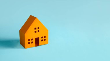 Canlı bir turuncu kağıt ev modeli, geniş bir kopya alanına sahip mavi bir arkaplanda izole edilmiş.