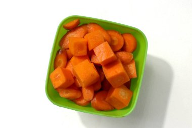 Beyaz arka planda izole edilmiş yeşil plastik bir kasede havuç dilimleri.