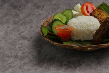 Lezzetli Endonezya yemeği, ayam bakar (kızarmış tavuk), bir tepsi beyaz pirinç, çıtır kraker, tempeh ve domates gibi taze sebzelerle servis edilir.