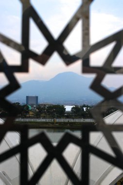 A breathtaking view of Mount Manglayang, an inactive volcano in West Java, Indonesia, framed by an intricate Islamic window design. clipart