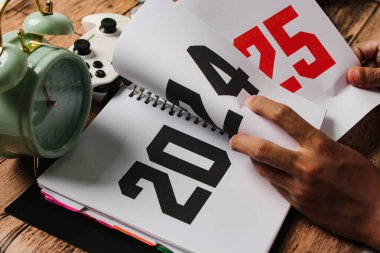 Bir insanın elinin bir defterin sayfalarını çevirirken yakın plan görüntüsü, 2024 yılı sayfada görünür ve kırmızı ile işaretlenmiş 