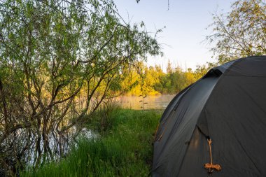 Yazın gün doğumunda nehrin kıyısında bir çadır kurun. Yüksek kalite fotoğraf