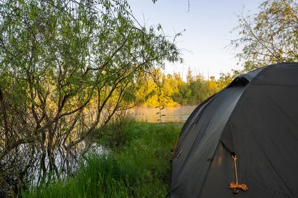 Yazın gün doğumunda nehrin kıyısında bir çadır kurun. Yüksek kalite fotoğraf