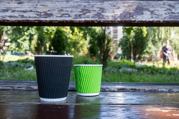 Two paper coffee cups stand on a wooden bench close-up. High quality photo