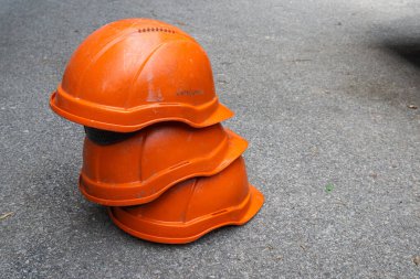 Üç tane turuncu inşaat kaskı üst üste istiflenmiş şekilde yerde yatıyor. Yüksek kalite fotoğraf