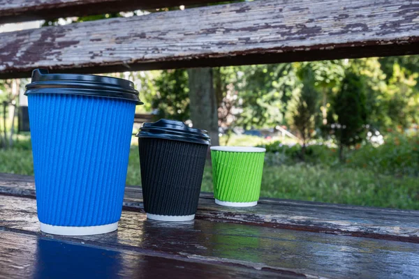 Three paper coffee cups with lids stand in a row on a wooden bench. Shot close-up, glasses of different sizes. High quality photo