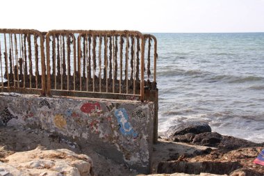 Üzerinde modern mozaik desenler ve alglerle kaplanmış metal tırabzanlar olan eski duvarlı kayalık bir sahil.
