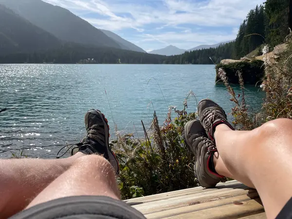 bare legs of a man and woman with hiking shoes relaxing with a view of the sunny landscape and mountain lake
