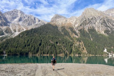 hiker on walking towards an emerald green mountain lake surrounded by high alpine mountains clipart