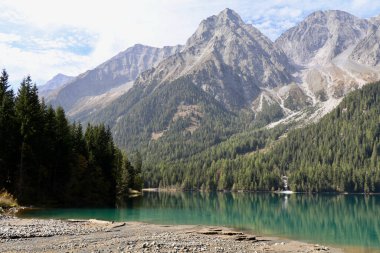 emerald mountain lake with pebble beach and surrounding high mountain range clipart