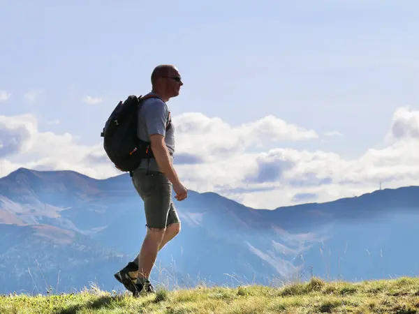 hiker with a day pack walking in a green mountain meadow with hazy blue mountains in the distance