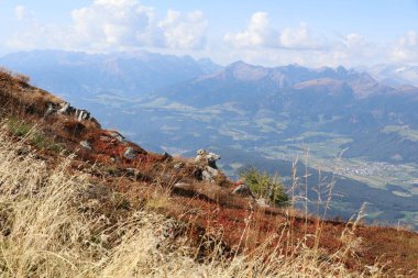 panoramic view of mountains near and far with in the front a rocky mountain meadow with bog bilberry plants coloring red in fall colors clipart