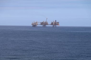 open sea on a clear day with an active oil rig on the horizon clipart