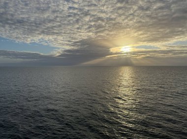 Bulutlu bir gökyüzü ve güneş gökyüzündeki bir delikten içeri giriyor.