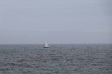 Lone sailboat on a vast empty ocean in misty conditions clipart