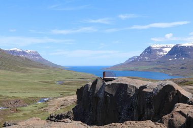 viewing platform on top of a rock formation overlooking a mountain stream and a panoramic view of the green mountains and blue fjord in the distance clipart