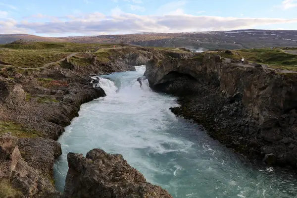 Volkanik kayalarla İzlanda manzarası ve uzaktaki Godafoss şelalesi ile Skalfandafljot nehrinin hızlı akan suyu.