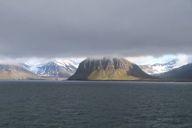 Alçak asılı kara bulutlar okyanusu gölgede bırakırken uzaktaki kıyı şeridi hala güneşte yüzüyor.