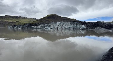 Geri çekilen Solheimajokull buzulunun panoramik görüntüsü ve buzul gölünün sularındaki yansıması.
